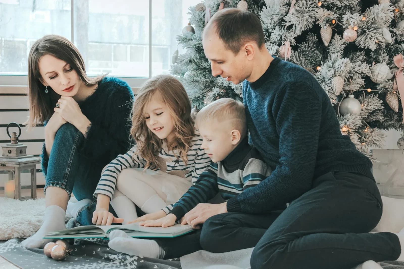A family reading together on the floor beside their Christmas tree